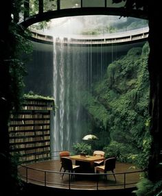 a table with two chairs and an umbrella in front of a waterfall filled with books