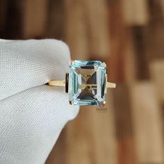 a ring with an aqua topazte surrounded by gold and diamond accents on a white gloved hand