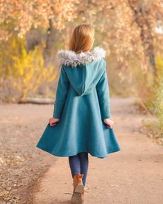 a woman walking down a dirt road wearing a blue coat with fur collar and cuffs