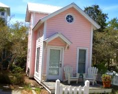 a small pink house with a white picket fence around the front door and porch area