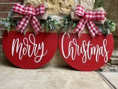 two red christmas signs sitting on the side of a building with bows and greenery