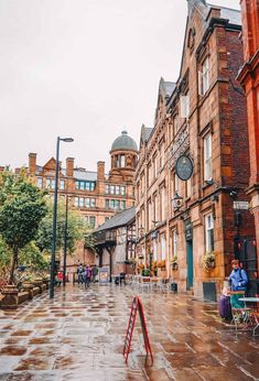 people sitting at tables in the middle of an old city street with tall brick buildings