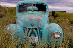 an old blue truck sitting in tall grass