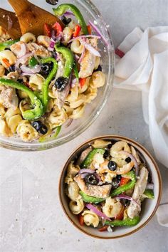 two bowls filled with pasta salad next to a wooden spoon and white cloth on the table