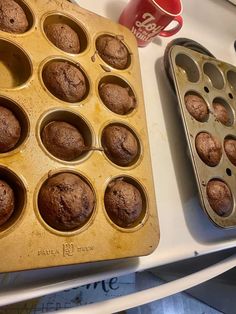 muffins in a pan next to a coffee mug and cupcake tin on a counter