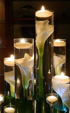 candles are lit in glass vases with flowers and leaves on the bottom one is filled with water