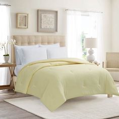 a bed with white sheets and yellow comforter in front of a window on top of a rug