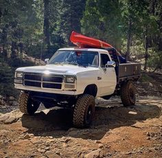 a white truck with a red kayak on the roof driving down a dirt road