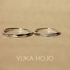 two wedding rings sitting next to each other on top of a brown surface with the words yuka hojo written across it