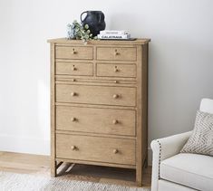 a wooden dresser sitting next to a white chair in a living room with a black vase on top of it