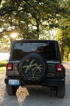 a black jeep with a palm tree painted on it's tire cover in the sun