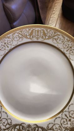 a white and gold plate sitting on top of a wooden table next to a brown chair