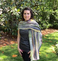 a woman standing in the grass wearing a multicolored shawl