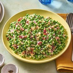 a yellow bowl filled with peas on top of a table next to silverware and forks