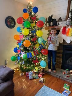 a young boy standing in front of a christmas tree decorated with balloons and streamers