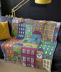 a couch with a colorful blanket on top of it next to a lamp and pillows