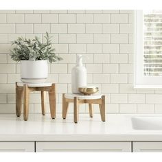 two small wooden stools sitting on top of a white counter next to a potted plant