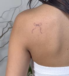 the back of a woman's shoulder with a small bow tattoo on her upper arm