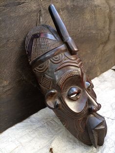 a wooden mask hanging on the side of a wall with a pen sticking out of it