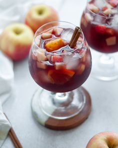 two glasses filled with liquid and fruit on top of a table next to apples, cinnamon sticks and napkins