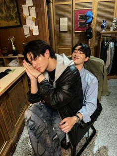 two young men sitting next to each other in an office area, one is covering his face with his hands