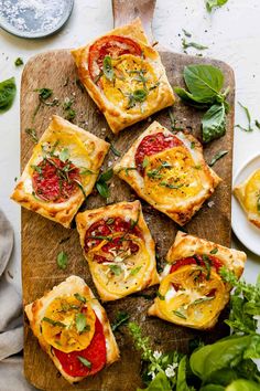 small pizzas with tomatoes and cheese on a cutting board next to fresh basil leaves