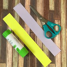 scissors and glue sitting next to each other on a wooden floor with strips of paper