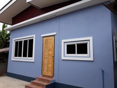 a blue house with two windows and steps leading up to the front door that is open