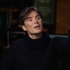 a man in a black turtle neck sweater holds his hand up