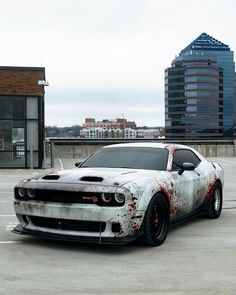 a white car with red paint on it parked in a parking lot next to tall buildings