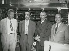 three men in suits and ties standing next to each other near an old fashioned machine