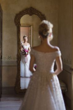 a woman in a wedding dress looking at herself in the mirror