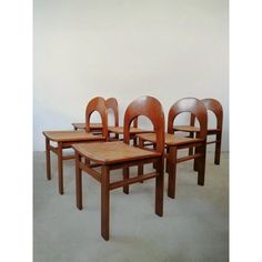 four wooden chairs sitting next to each other on top of a cement floor in front of a white wall