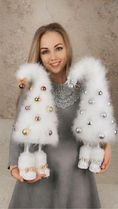 a woman in grey dress holding two white fur gloves with gold and silver decorations on them