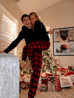 a man and woman are jumping in front of a christmas tree