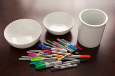 a group of markers sitting on top of a wooden table next to a white cup