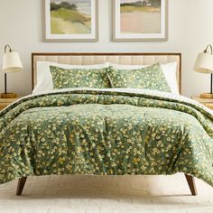 a bed with green and yellow flowers on it in a bedroom next to two pictures