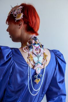 a woman with red hair wearing a blue dress and some necklaces on her neck