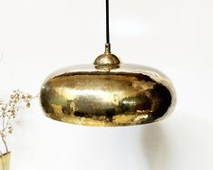 a gold colored light hanging from a ceiling next to a vase with flowers in it