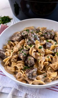 a white bowl filled with pasta covered in mushrooms and parsley next to a crock pot