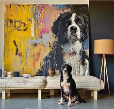 a black and white dog sitting on the floor next to a couch in front of a painting