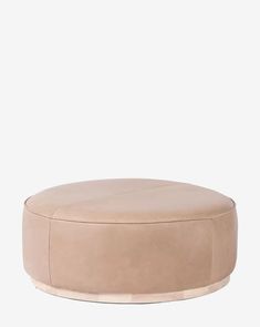 a round ottoman that is sitting on top of a white surface with a light brown leather cover