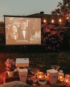 an outdoor movie is set up with popcorn buckets and candles in front of the screen