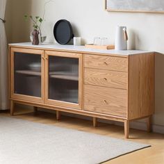 a wooden cabinet with glass doors in a living room next to a rug and potted plant