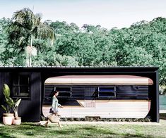 a woman walking past a trailer parked in front of a forest filled with palm trees