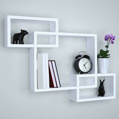 a white shelf with three shelves holding books and an alarm clock on the wall next to a cat figurine