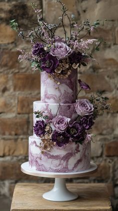 a three tiered cake with purple flowers and greenery