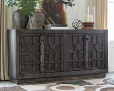 a large wooden cabinet sitting on top of a rug next to a vase filled with flowers