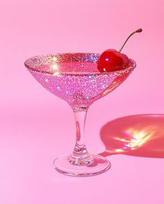 a pink martini glass with a cherry on the rim and sparkles in the bottom