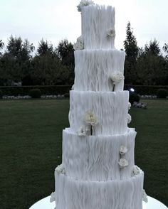 a white wedding cake with flowers on it sitting in the middle of a field next to some trees